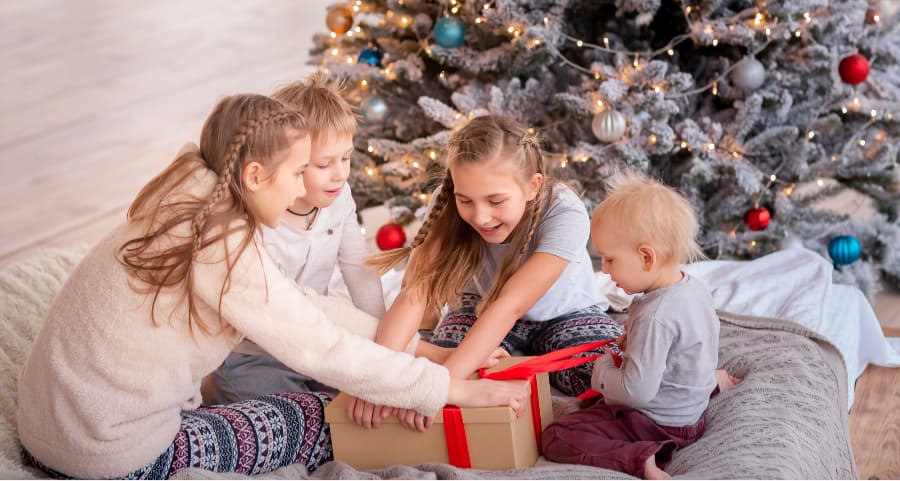 Kids opening a gift in the living room next to a Christmas tree.